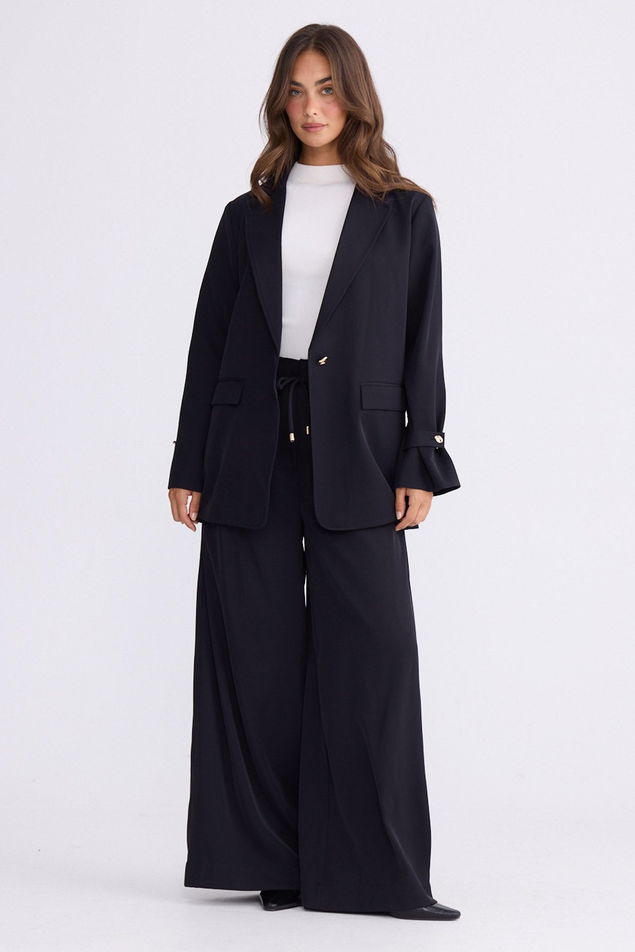 Model wearing Kensington Blazer in black with notched lapels and long sleeves, front view on white background