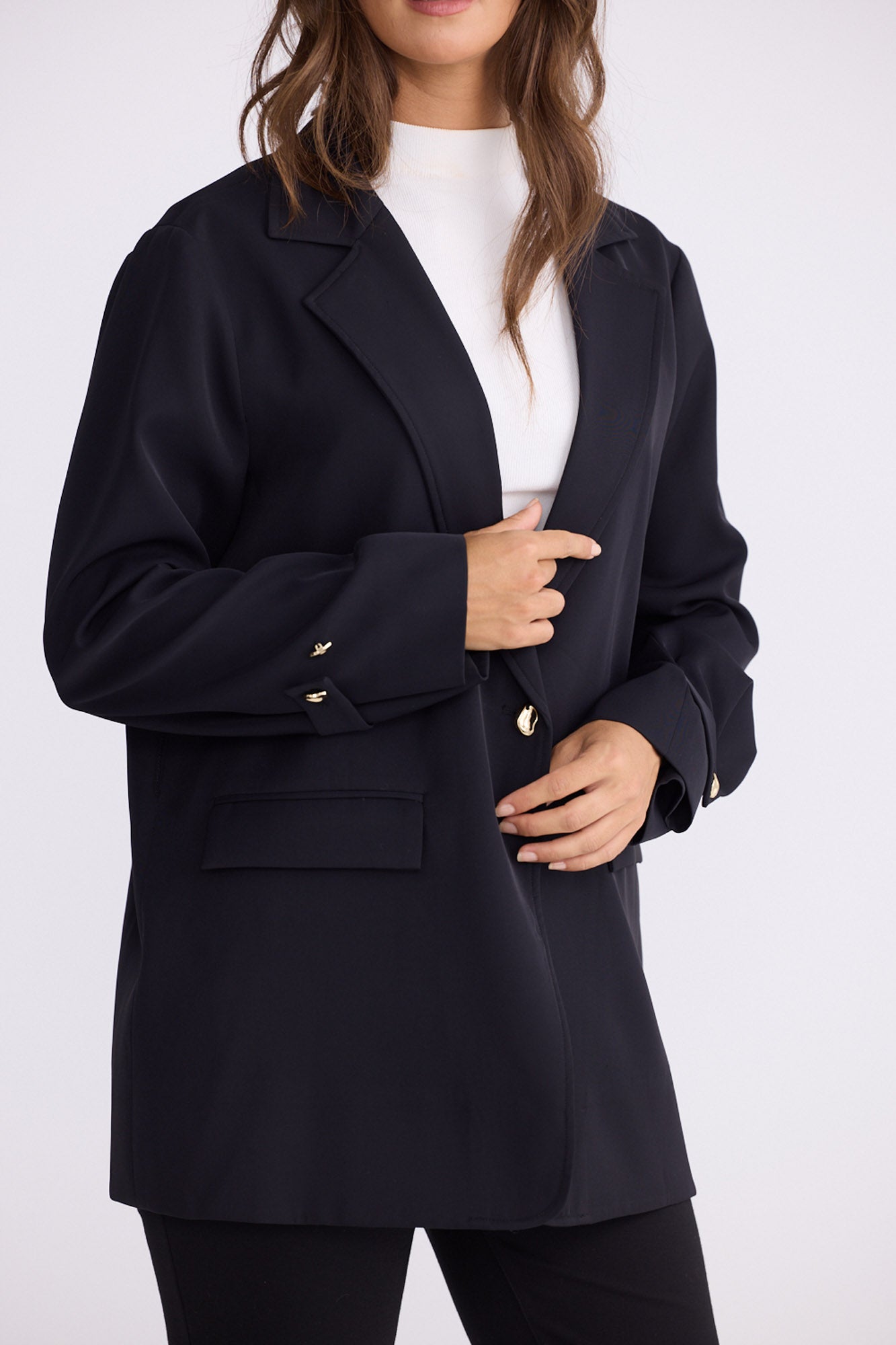 Model wearing Kensington Blazer in black with notched lapels and long sleeves, side view on white background