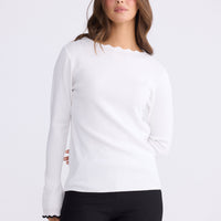 Woman wearing a white long-sleeve top and black pants on white background