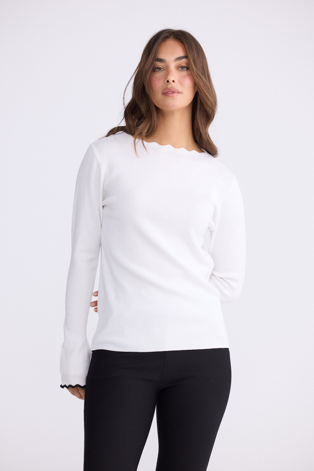 Woman wearing a white long-sleeve top and black pants on white background
