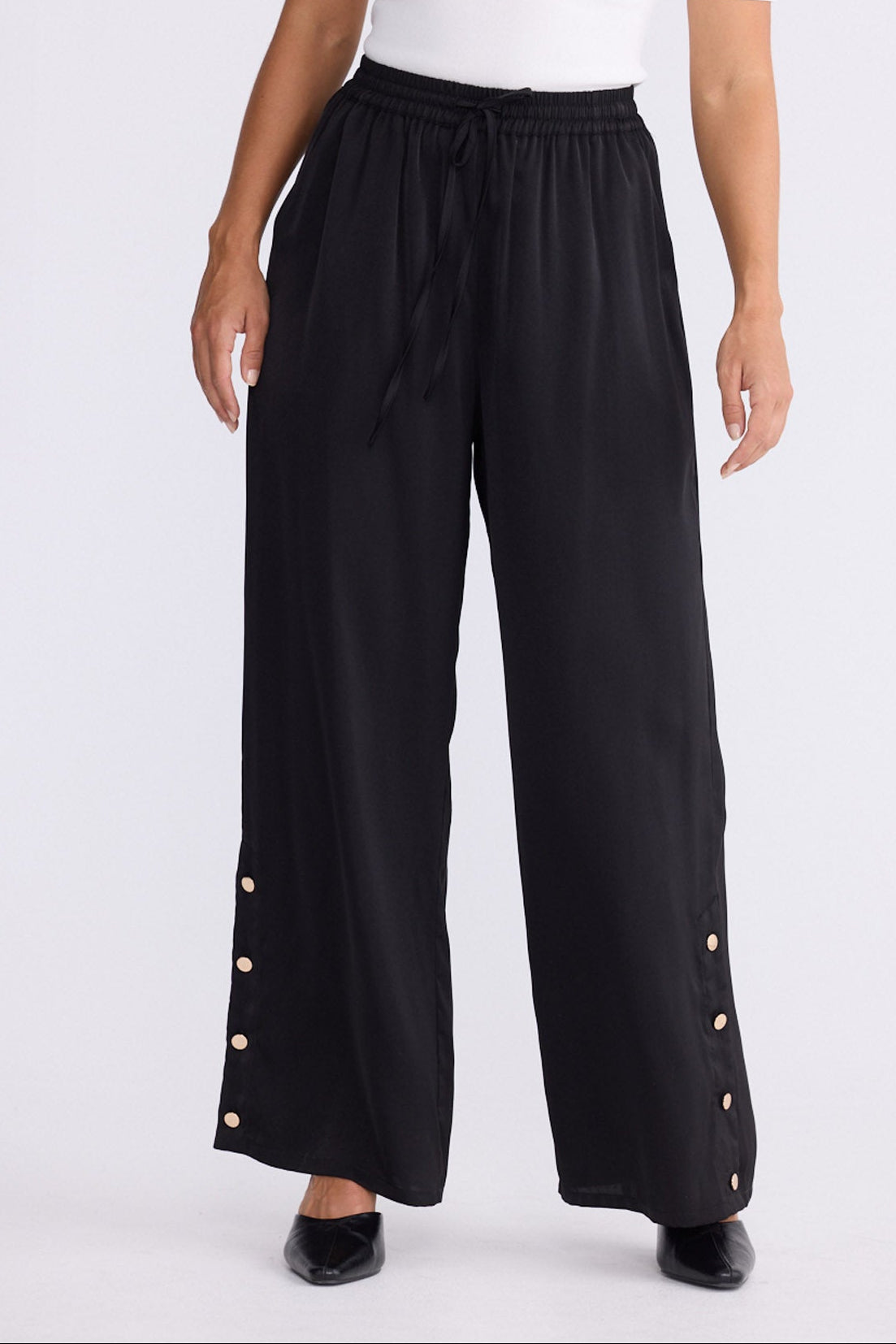 Model wearing Cassian Pant black pants with cutaway hip pockets, alternate studio view on white background