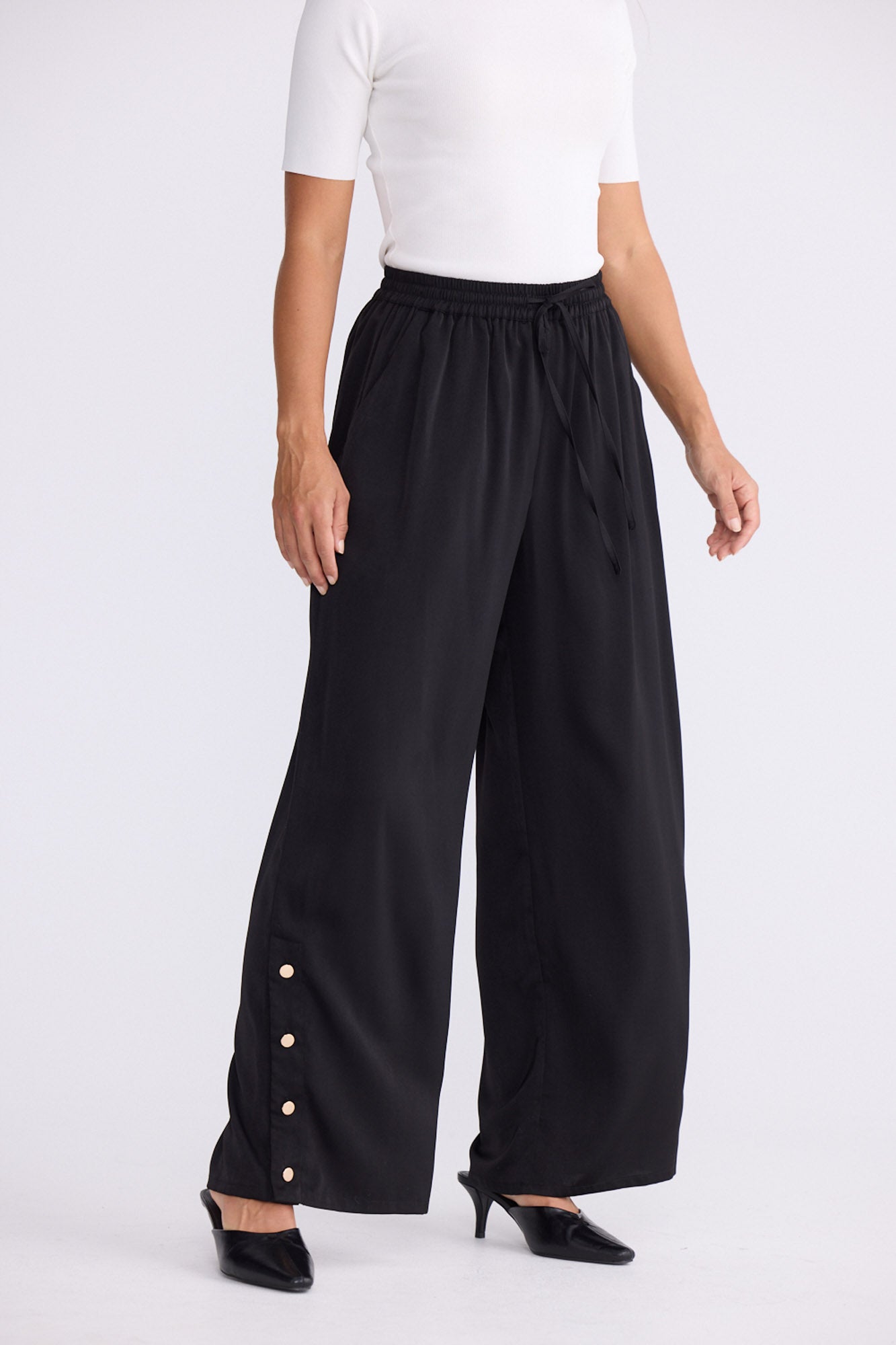 Model wearing Cassian Pant black pants with cutaway hip pockets, alternate studio view on white background