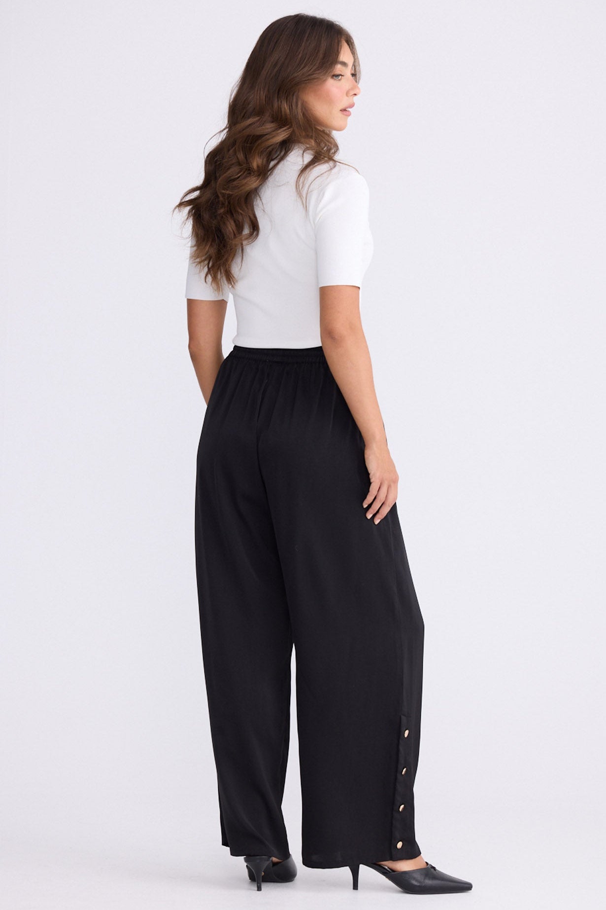 Model wearing Cassian Pant black pants with cutaway hip pockets, front view on white background