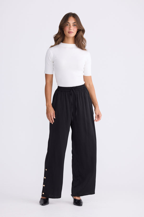Woman wearing a white top and black wide-leg pants on a white background