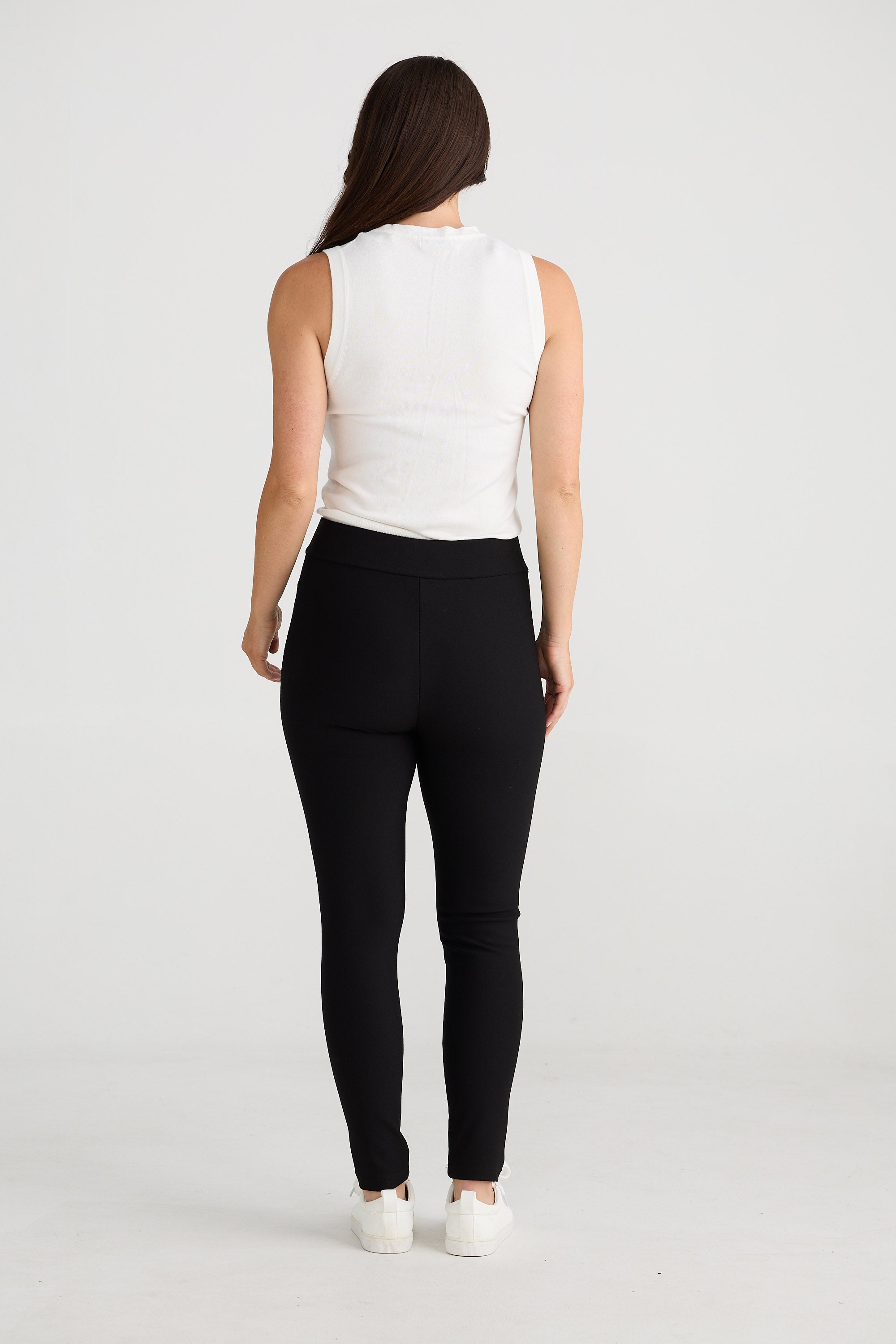 Woman wearing a white sleeveless top and black leggings on a white background