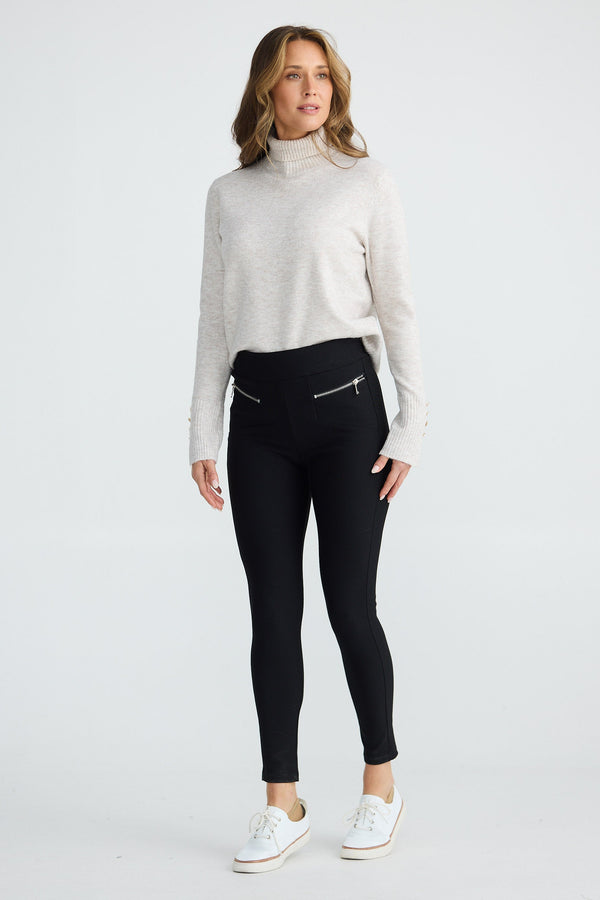 Woman wearing a white turtleneck sweater and black leggings on a white background