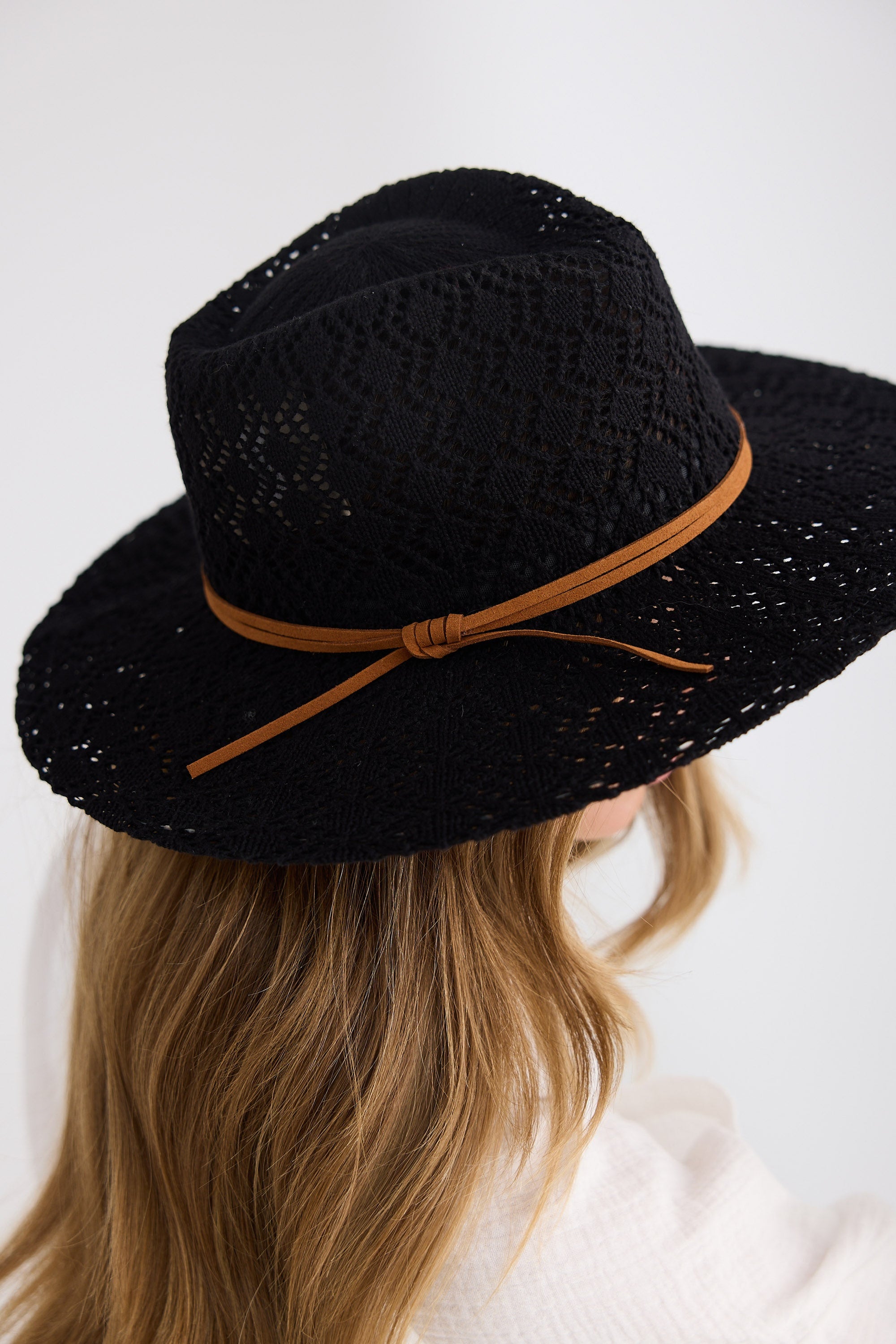 Black hat with a brown band worn by a person on a white background