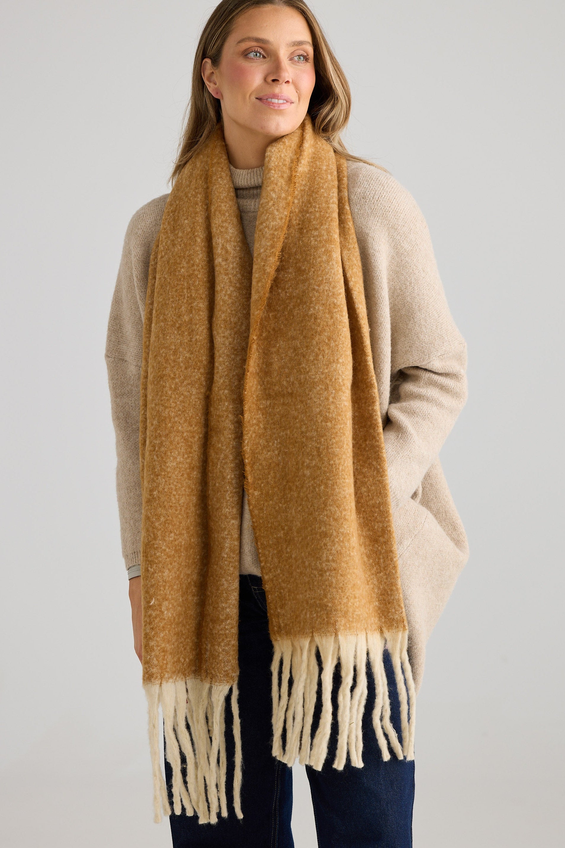 Woman wearing a mustard yellow scarf with fringes on a plain background