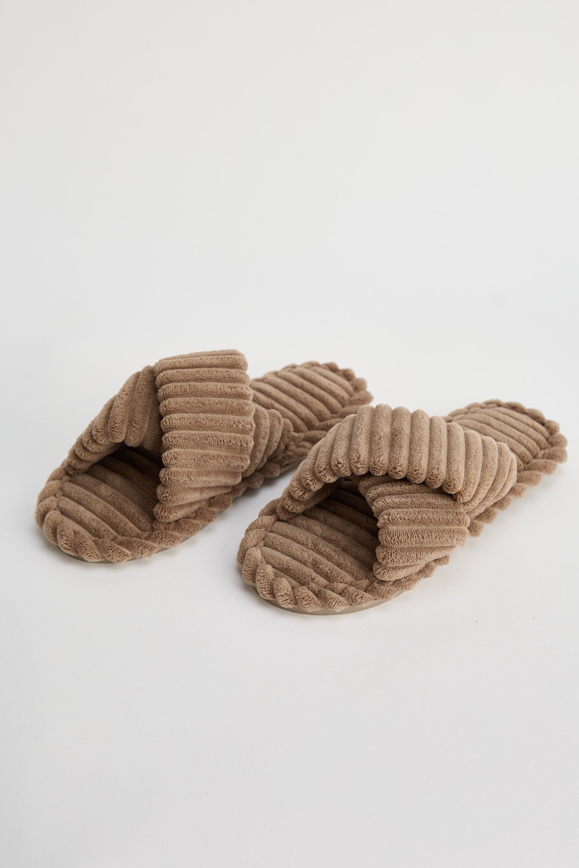 Pair of ribbed brown slippers on a light gray background