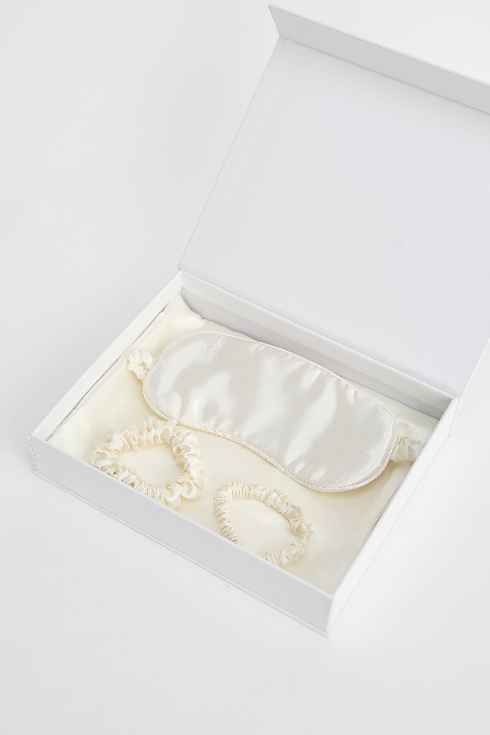 White satin eye mask in an open white box on a light gray background