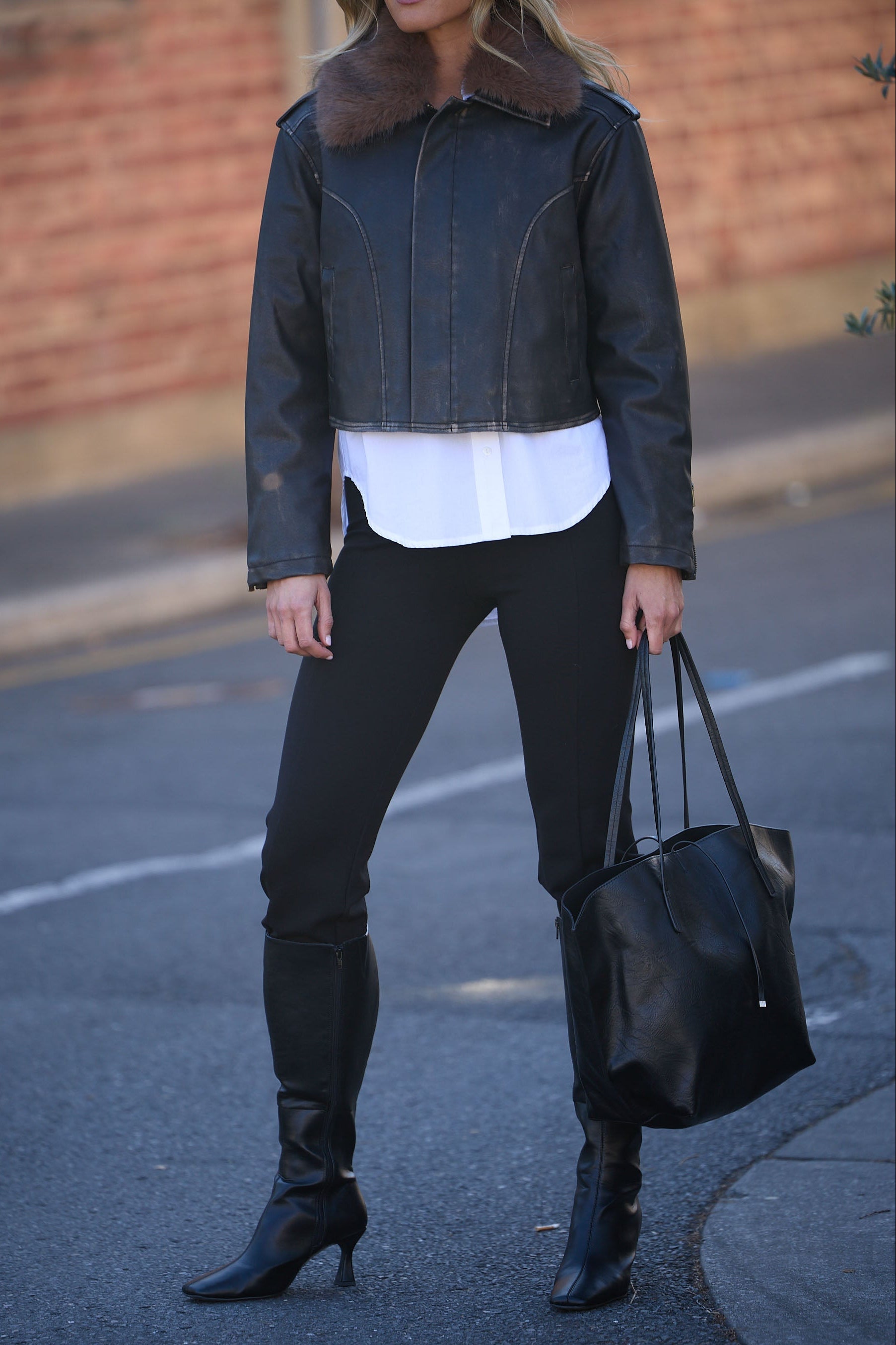 Person wearing a black leather jacket, white shirt, black pants, and black boots on a street.
