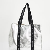 Silver tote bag with black straps featuring 'everywoman' on a white background