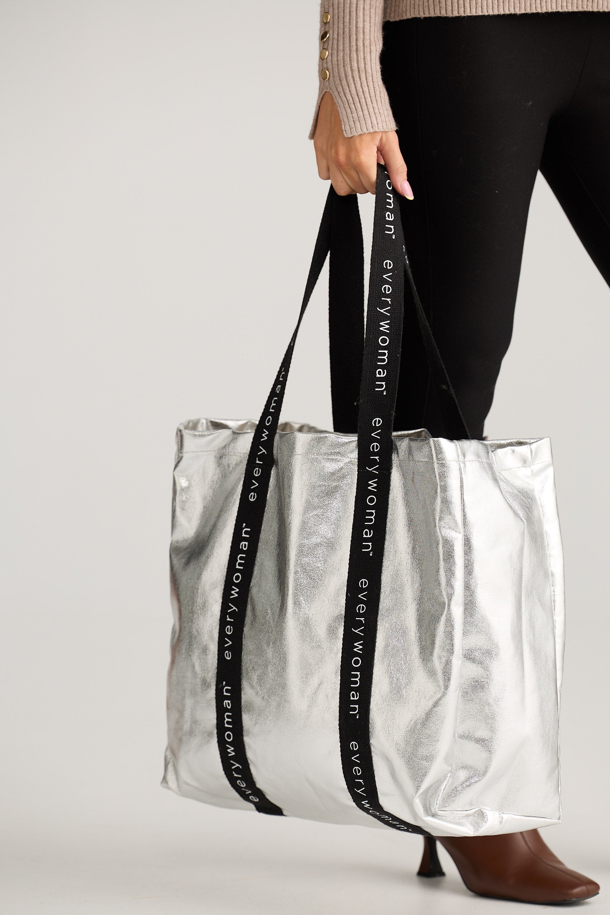 Person holding a clear tote bag with a black strap featuring 'everywoman' branding.