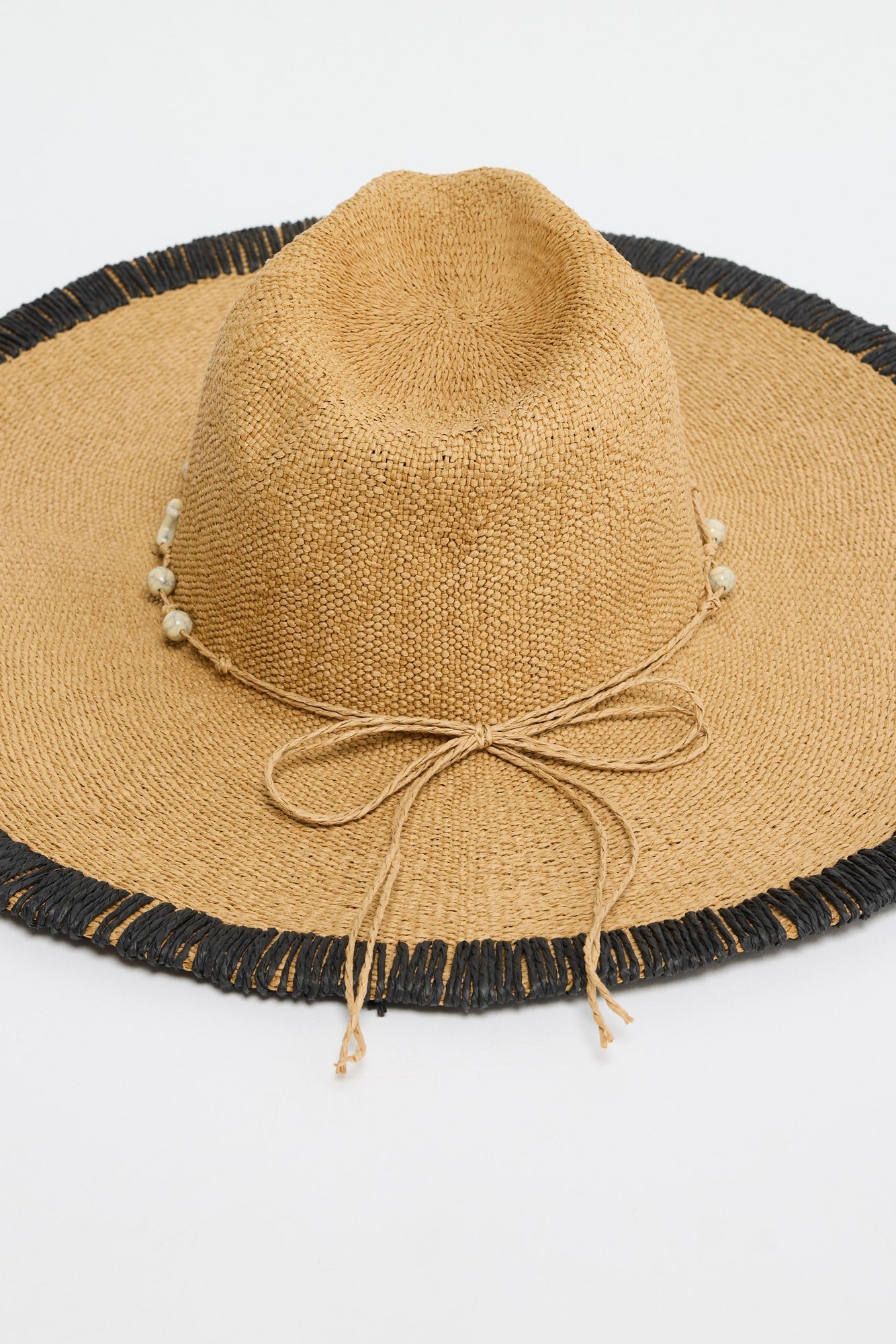 Close-up of the Carlitta Hat's woven texture, black fringed brim trim and beaded raffia tie