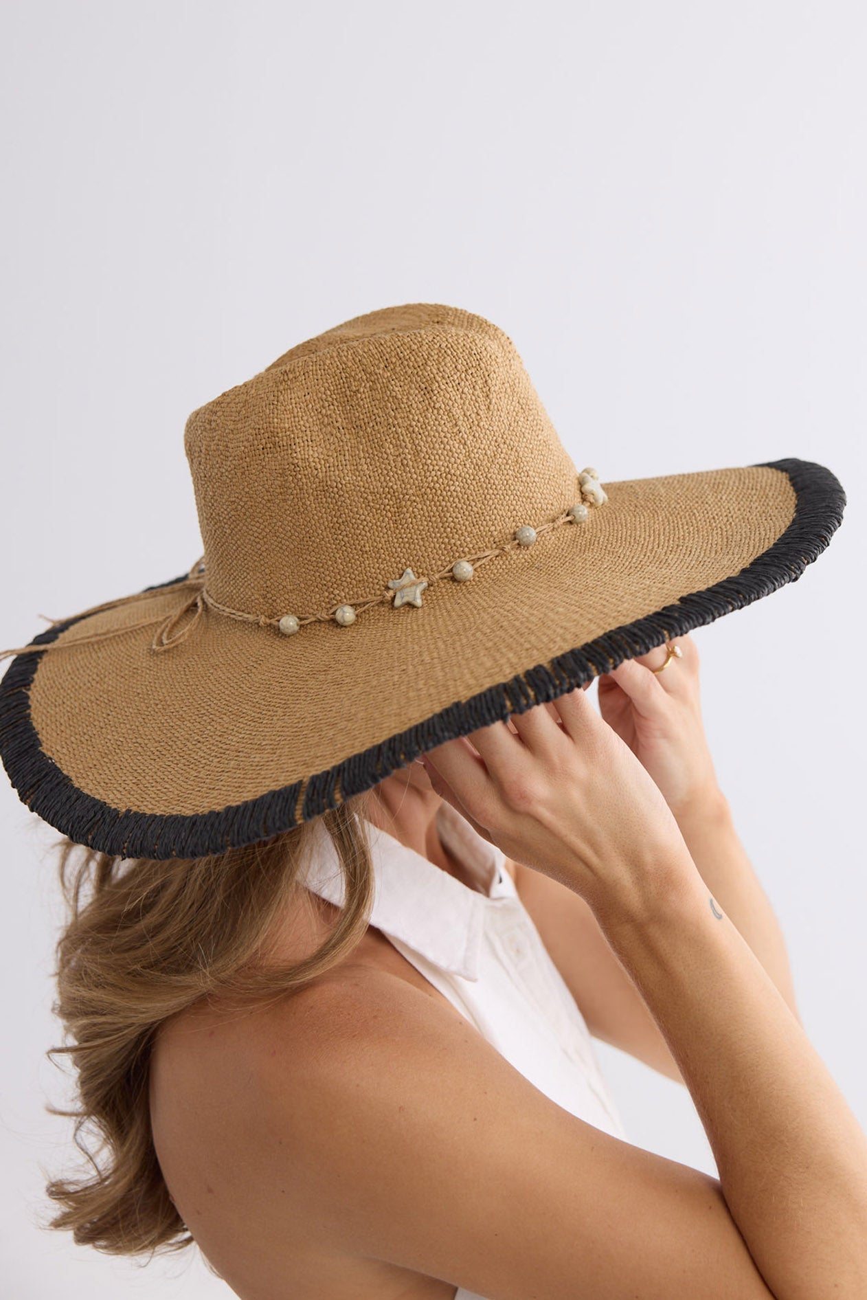 Overhead back view of the Carlitta Hat showing the black fringed brim and beaded raffia tie, worn with a white sundress