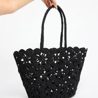 Large open-weave black crochet tote basket with twisted rope handles, shown held by hand against a white background