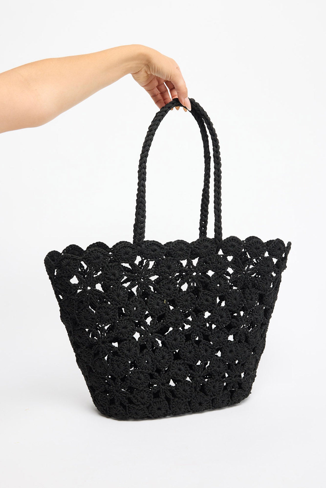 Large open-weave black crochet tote basket with twisted rope handles, shown held by hand against a white background