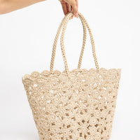 Large open-weave taupe crochet tote basket with twisted rope handles, shown held by hand against a white background