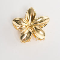 Frangi Hair Claw in gold - flat lay view of the plumeria flower-shaped metal hair claw