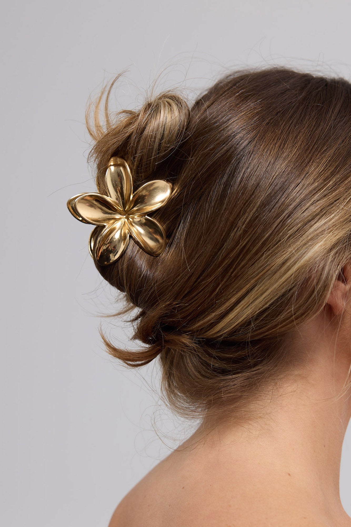 Frangi Hair Claw in gold worn in a low hair bun, showing the flower claw securing an updo