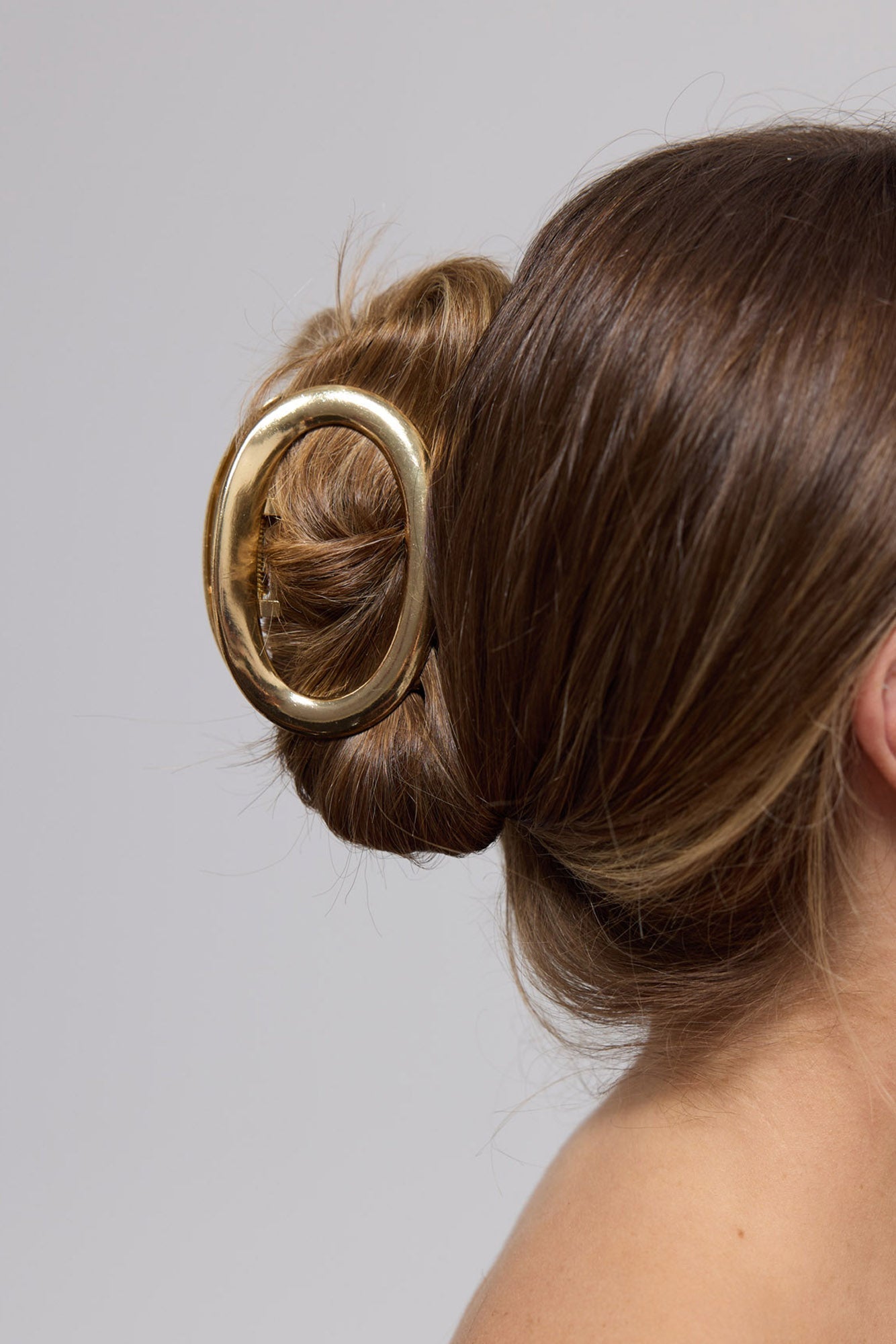 Noosa Hair Claw in gold worn in a low bun, showing the oval claw securing the hair