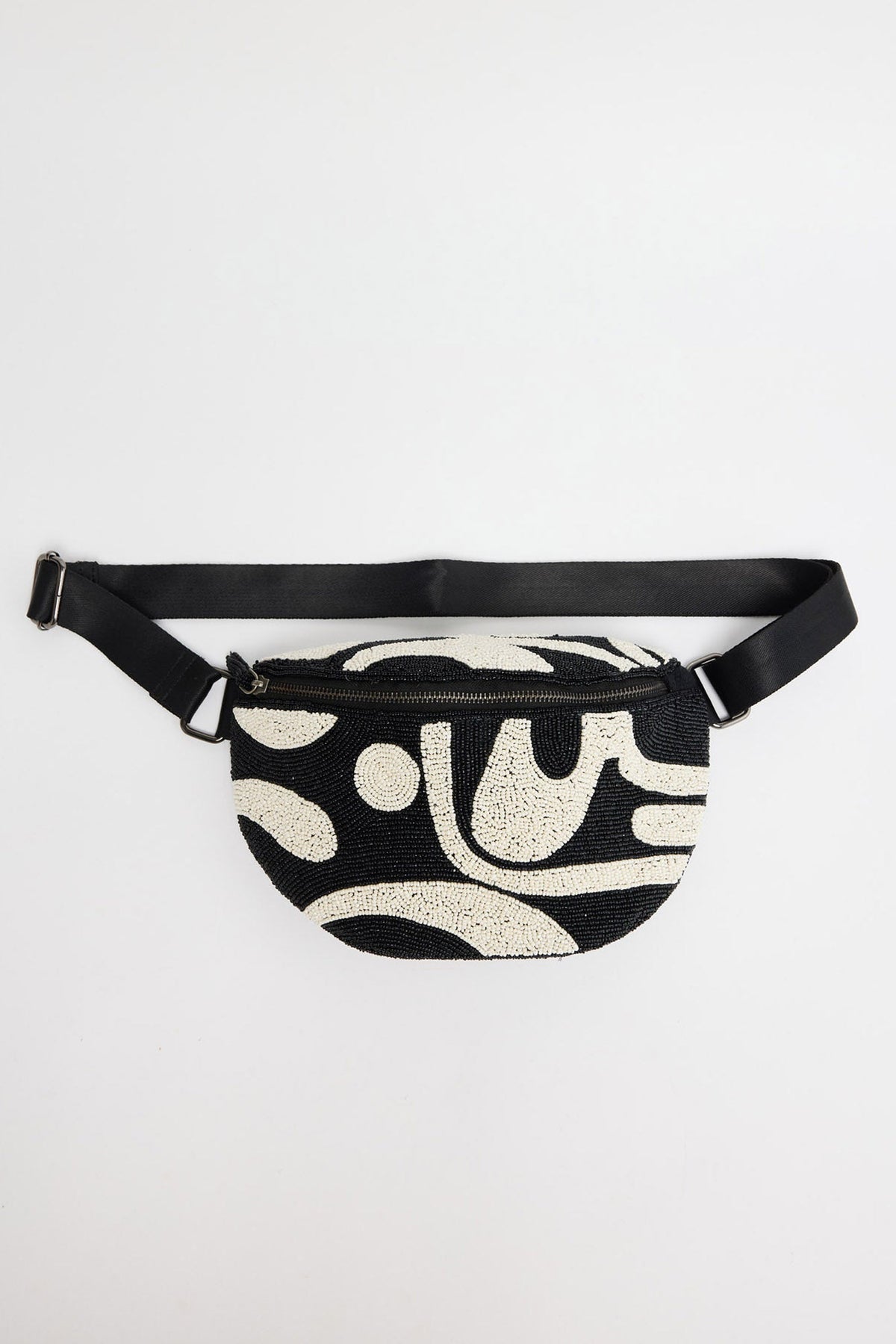 Semi-circular beaded bumbag fully covered in black and white seed beads in an abstract swirl and wave pattern, with a black adjustable nylon strap and zip closure, shown flat on a white background