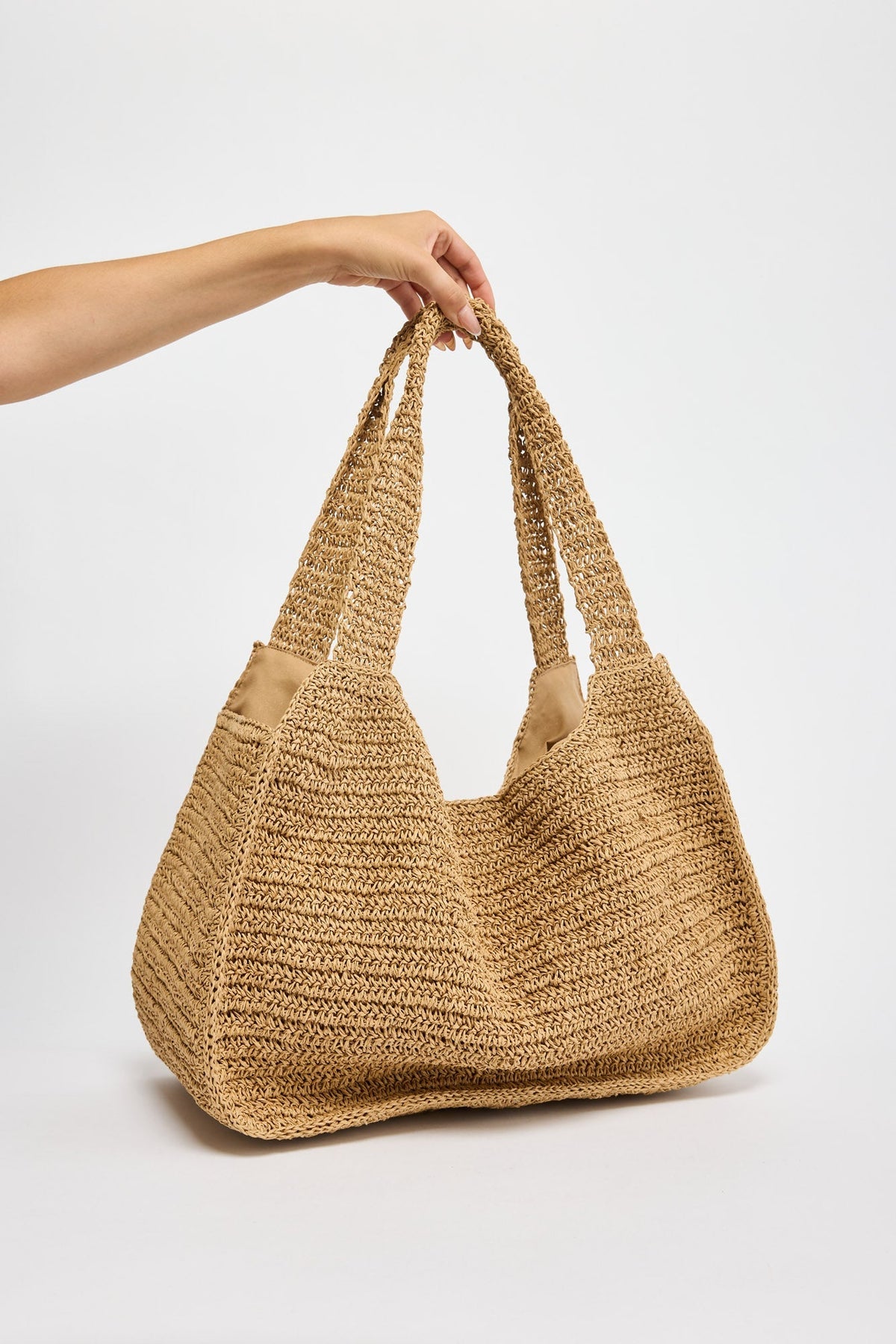 Large slouchy hobo bag in chunky natural tan woven raffia with braided rope handles, held by hand against a white background