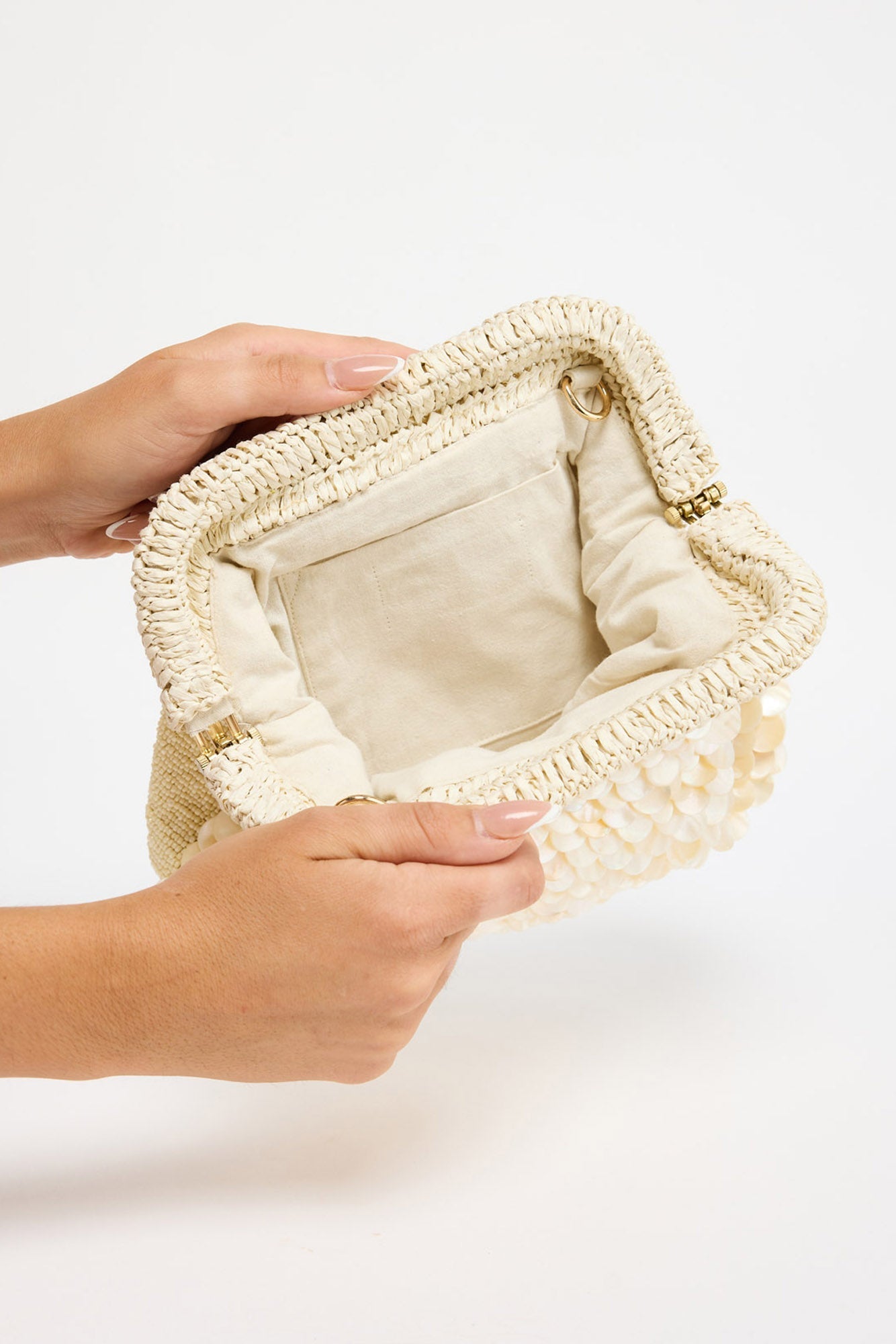 Sandy Clutch in creme held open in both hands, showing the interior lining and D-ring detail