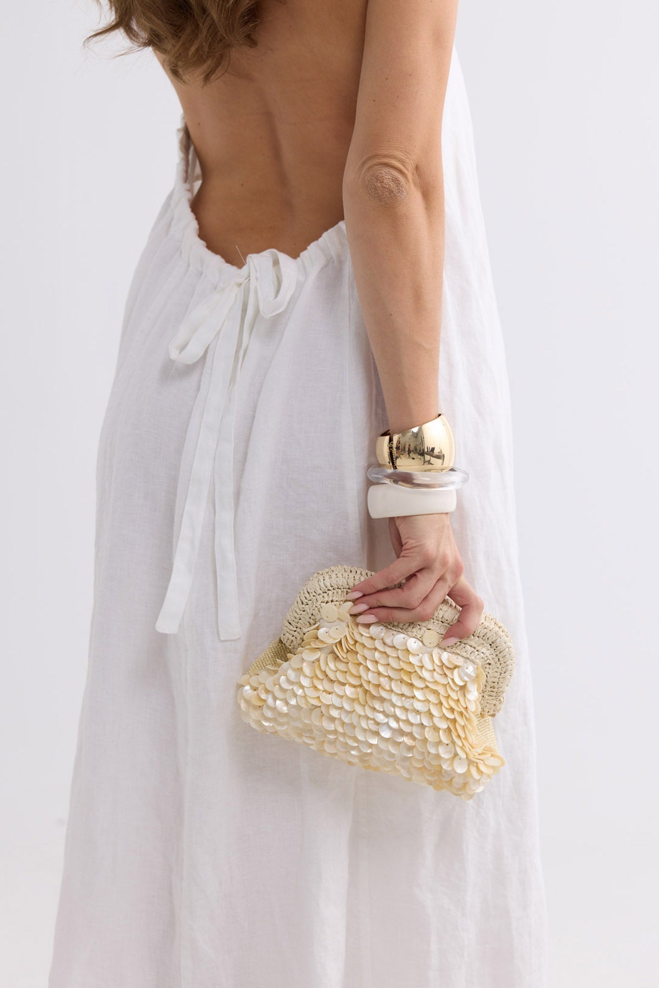 Sandy Clutch in creme held behind the back, worn with a backless white linen dress