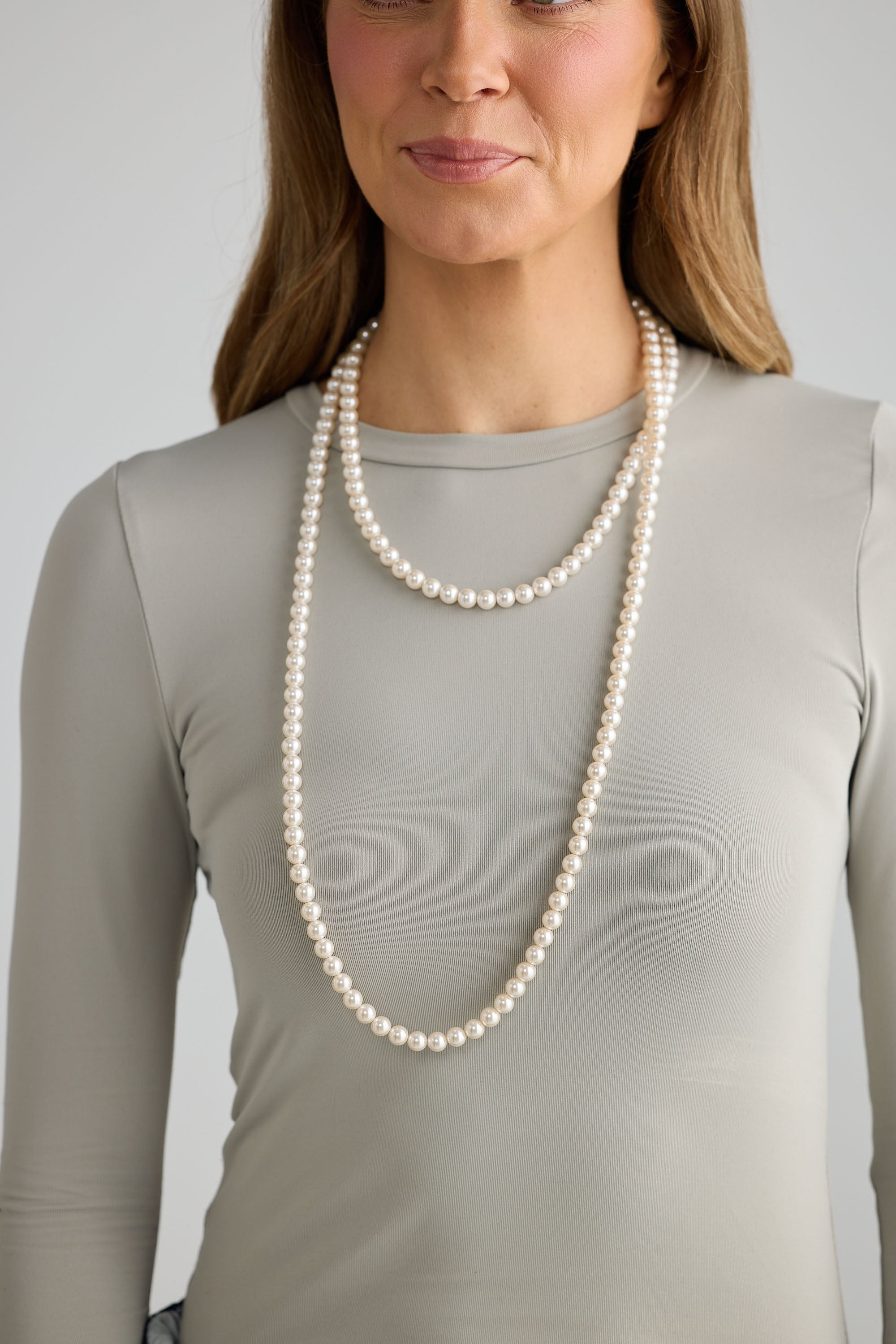 Woman wearing a long pearl necklace against a plain background