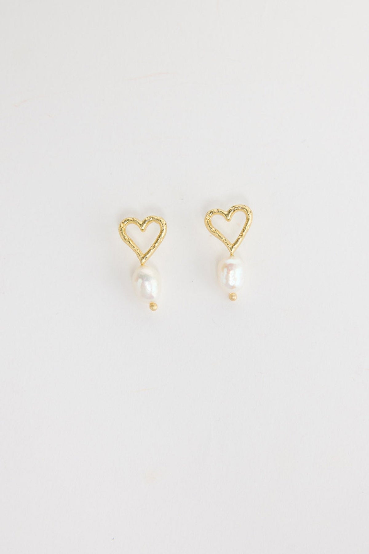 Pair of gold-tone open heart stud earrings with a single freshwater pearl drop and a small gold bead below, laid flat on a white background