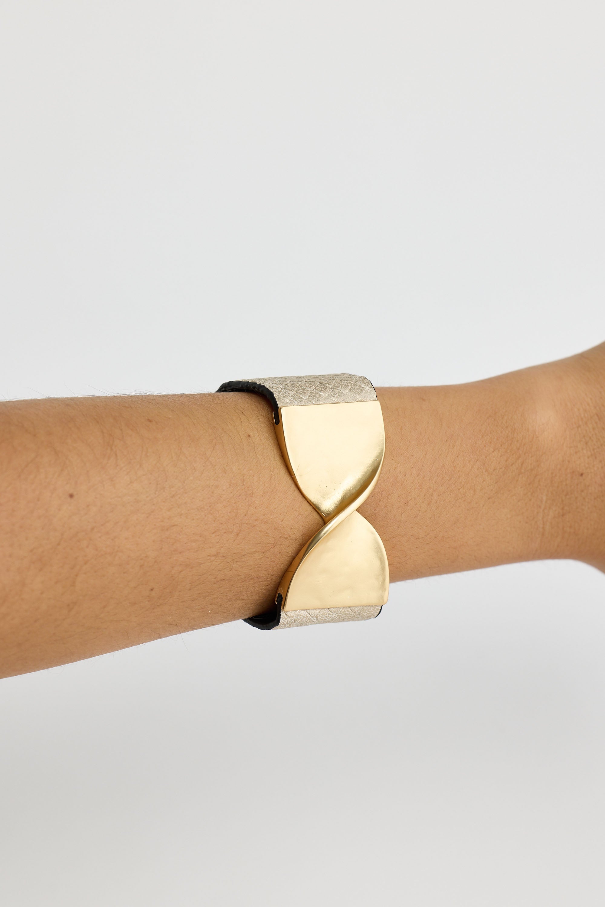 Gold bracelet on a wrist against a light gray background