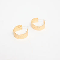 Annabel Earrings in gold – pair of hammered-finish gold-tone huggie hoop earrings laid flat
