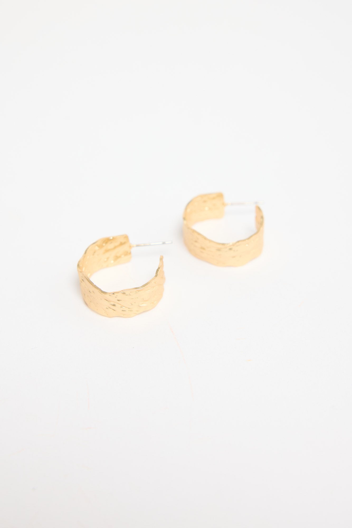 Annabel Earrings in gold – pair of hammered-finish gold-tone huggie hoop earrings laid flat