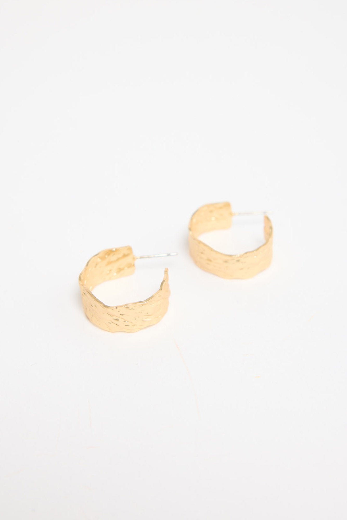 Close-up of Annabel gold hammered huggie hoop earrings showing the textured metal finish and post backs