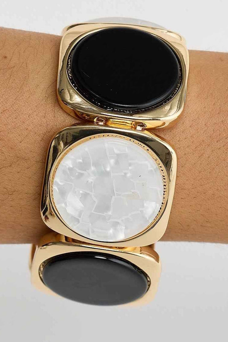 Gold bracelet with black and white stones on a wrist against a light gray background