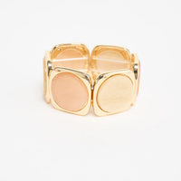 Gold-tone stretch bracelet with alternating square panels set with salmon-pink and cream resin discs, shown flat on a white background