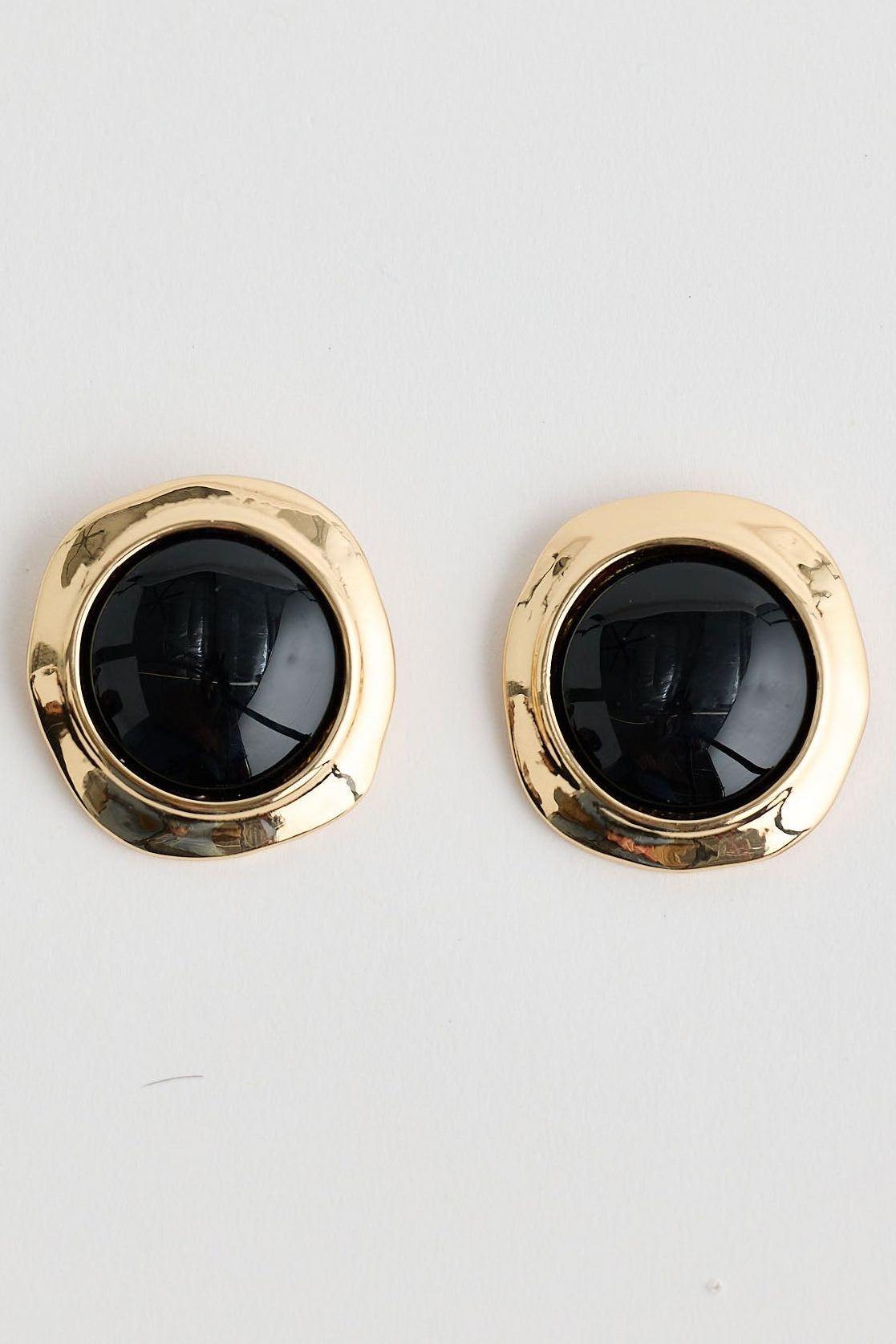 Pair of gold earrings with black stones on a light gray background