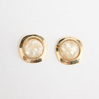 Pair of large square gold-tone stud earrings each set with a round cream mother-of-pearl resin stone in a hammered bezel, laid flat on a white background