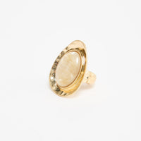 Large oval gold-tone adjustable statement ring with a cream mother-of-pearl resin stone set in a wide hammered bezel, shown at an angle on a white background