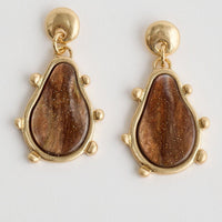 Pair of gold earrings with brown teardrop-shaped stones on a light gray background