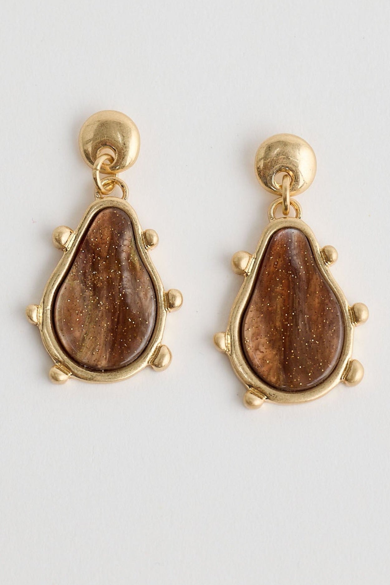 Pair of gold earrings with brown teardrop-shaped stones on a light gray background