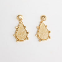 Pair of gold-tone drop earrings with a round ball stud and a teardrop-shaped cream resin pendant framed in gold with small ball accents, laid flat on a white background