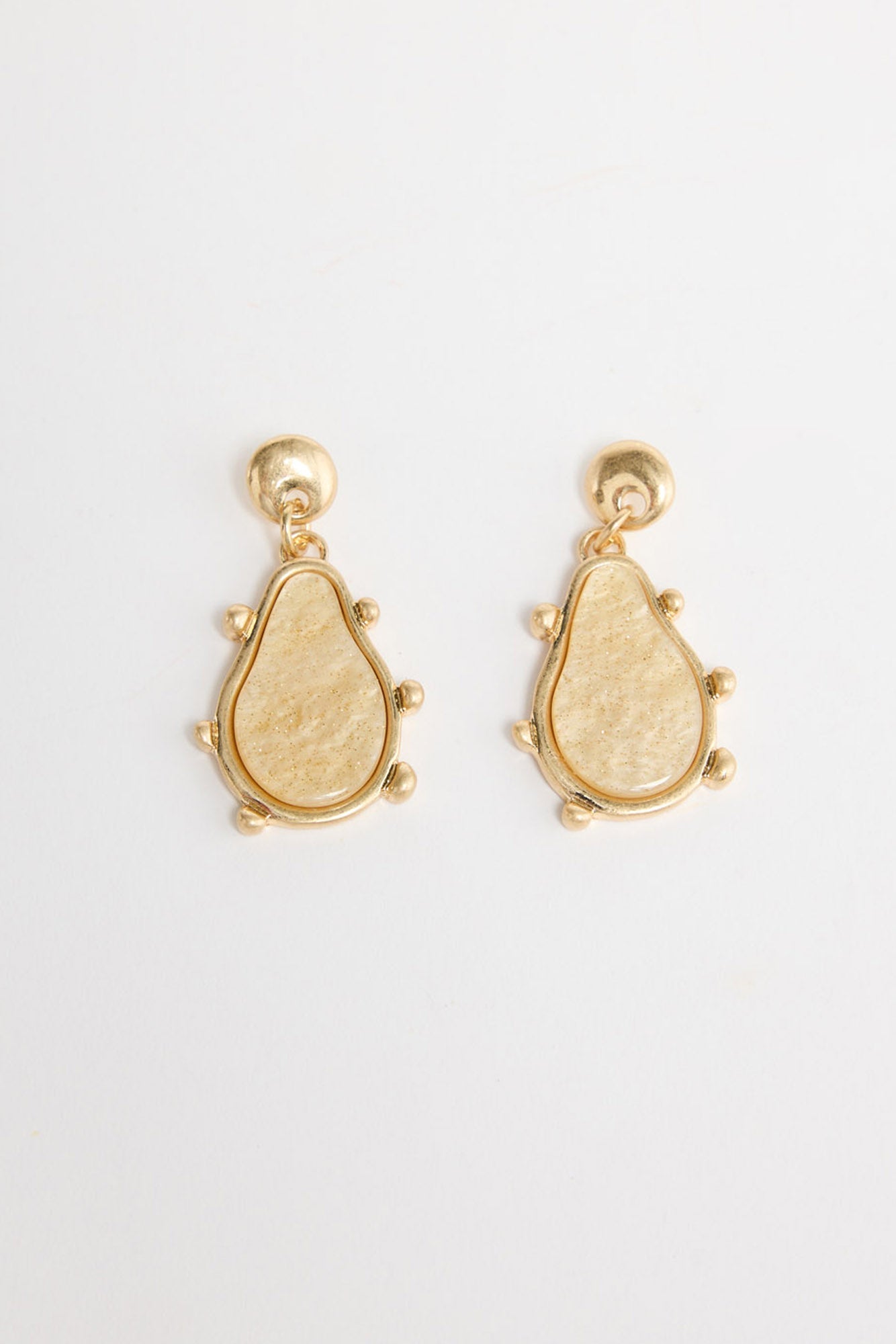 Pair of gold-tone drop earrings with a round ball stud and a teardrop-shaped cream resin pendant framed in gold with small ball accents, laid flat on a white background