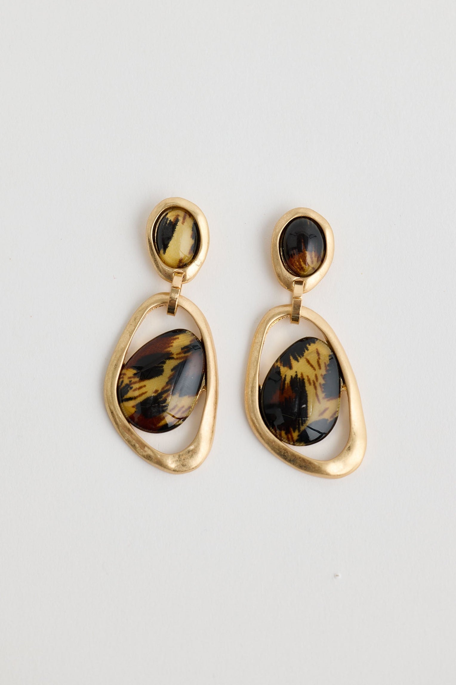 Pair of gold earrings with tiger eye stones on a light gray background