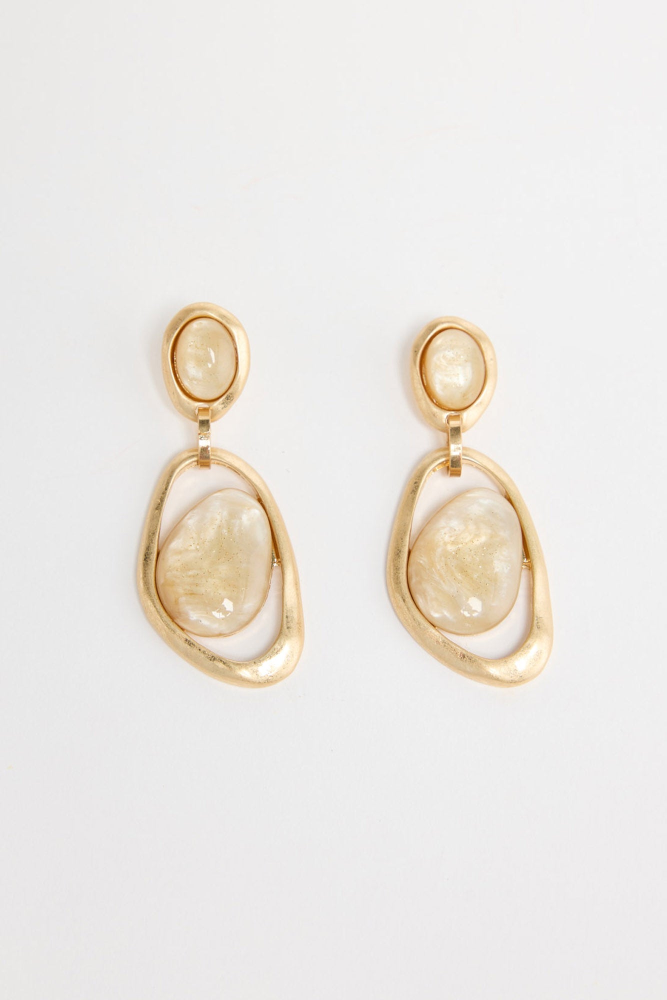 Pair of gold-tone drop earrings with a small oval cream resin stud and a large organic-shaped open gold hoop holding a cream resin stone, laid flat on a white background