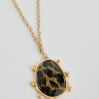 Gold necklace with a black and gold stone pendant on a light gray background