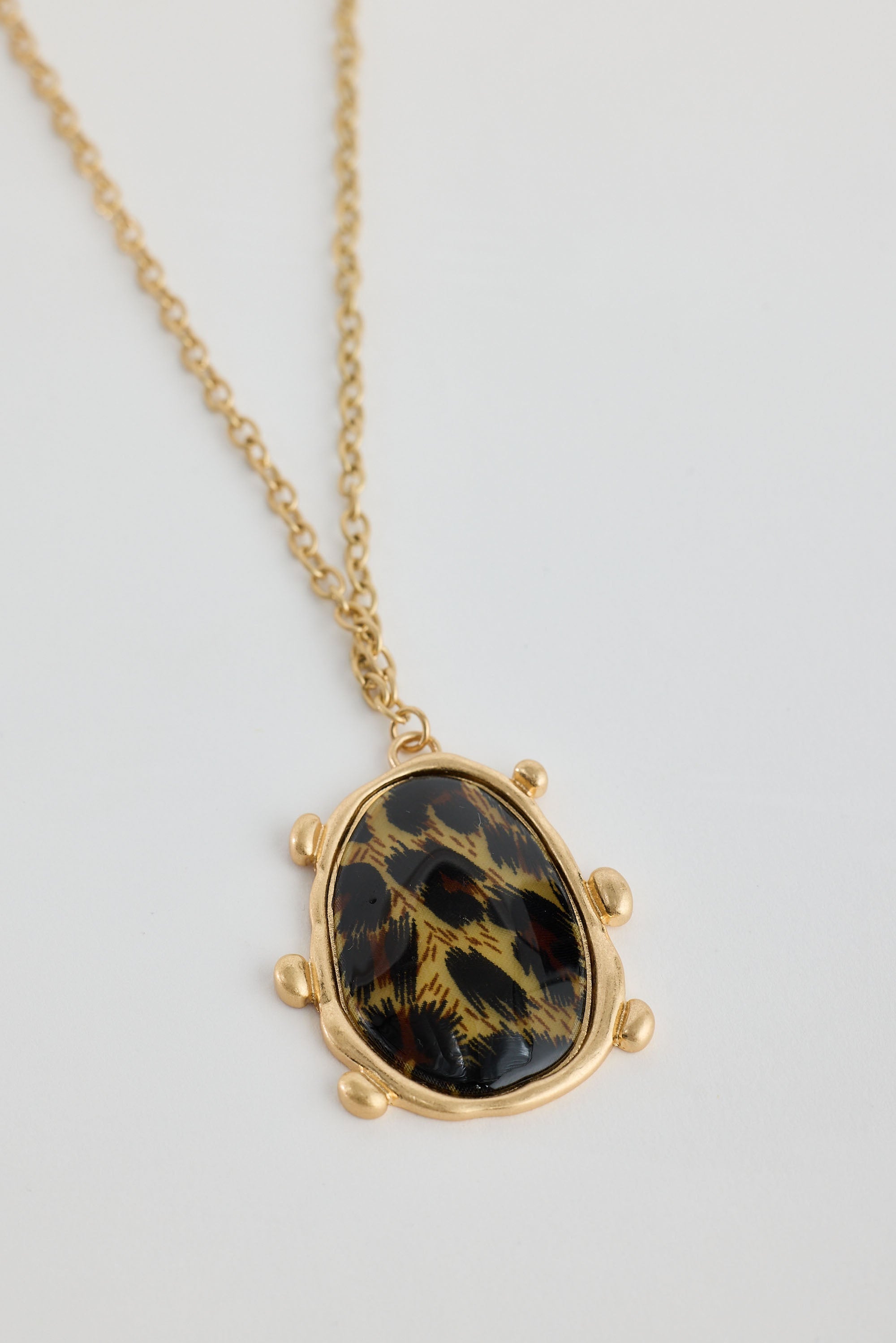 Gold necklace with a black and gold stone pendant on a light gray background