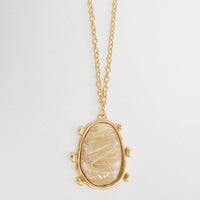 Gold-tone chain necklace with a large oval cream mother-of-pearl resin pendant set in a wide hammered bezel with small ball accents, shown flat on a white background