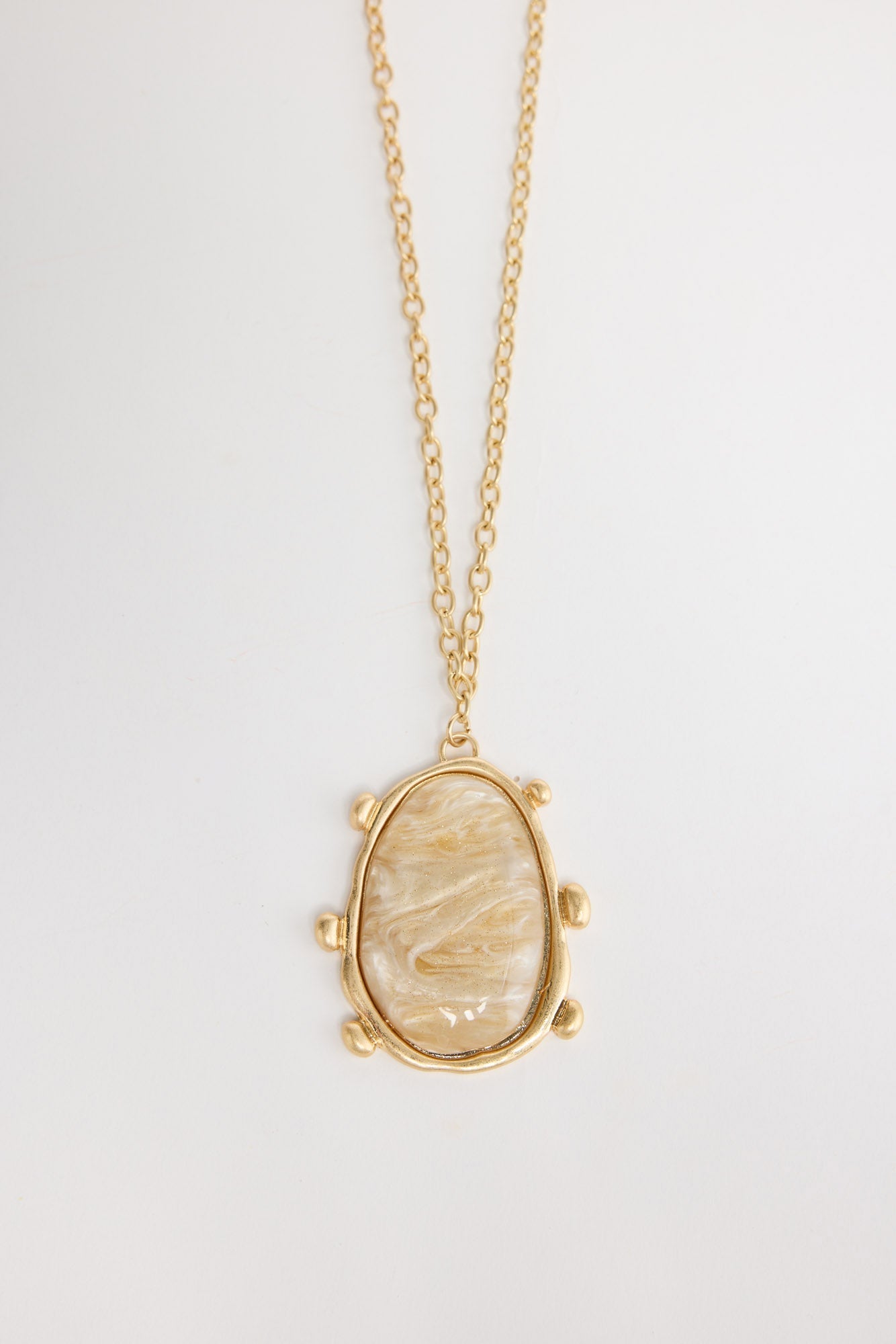 Gold-tone chain necklace with a large oval cream mother-of-pearl resin pendant set in a wide hammered bezel with small ball accents, shown flat on a white background